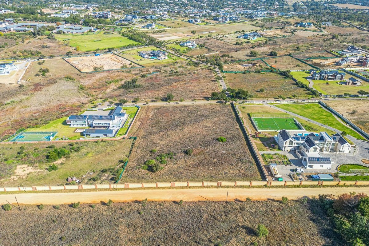 Aerial view of a vacant residential plot situated in a developed estate, featuring perimeter walling and direct access from a dirt road.