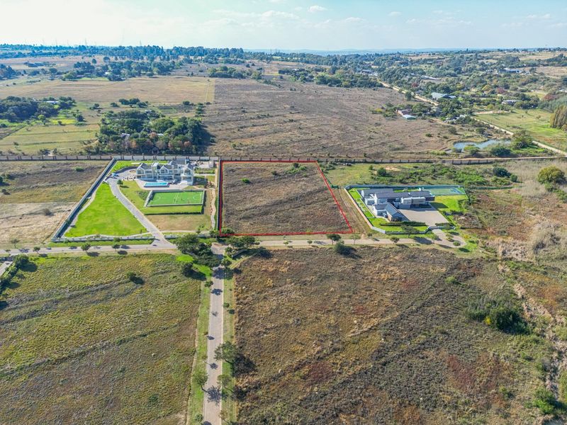 An aerial view of a vacant residential plot highlighted in red, situated within a developed estate with surrounding landscape.