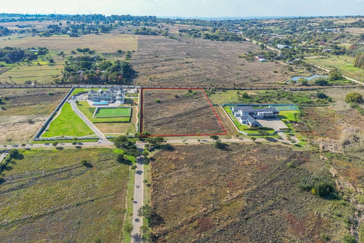 An aerial view of a vacant residential plot highlighted in red, situated within a developed estate with surrounding landscape.