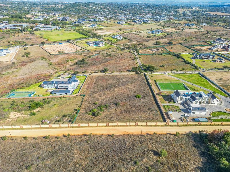 Aerial view of a vacant residential plot situated in a developed estate, featuring perimeter walling and direct access from a dirt road.