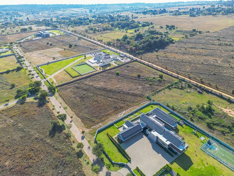 Aerial view of a residential property featuring a large landscaped garden, paved driveway, solar panels, and a private tennis court.