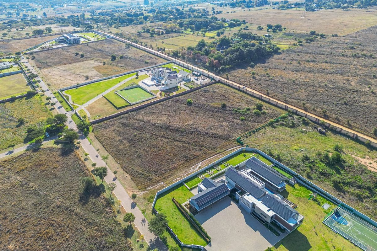 Aerial view of a residential property featuring a large landscaped garden, paved driveway, solar panels, and a private tennis court.