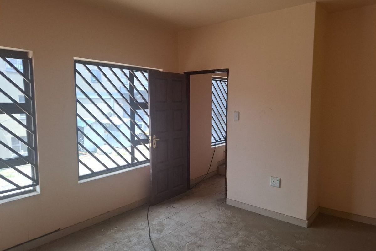 An empty interior room featuring tiled flooring, security bars on windows, and a wooden door leading to an adjacent space.