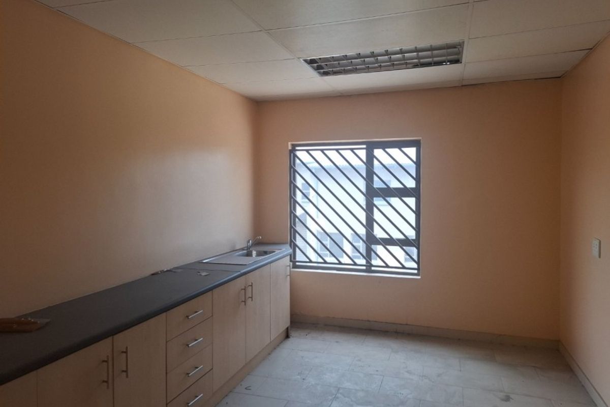 A functional, empty kitchenette featuring laminate cabinetry, a stainless steel sink, tiled flooring, and a drop ceiling with integrated lighting.