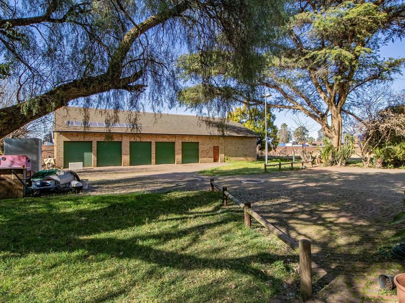 Rear view of the commercial property featuring a multi-bay garage with green roller doors, paved driveway, and mature trees.
