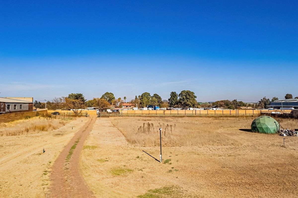 Aerial view of a large, undeveloped commercial plot featuring an unpaved access road and perimeter fencing.