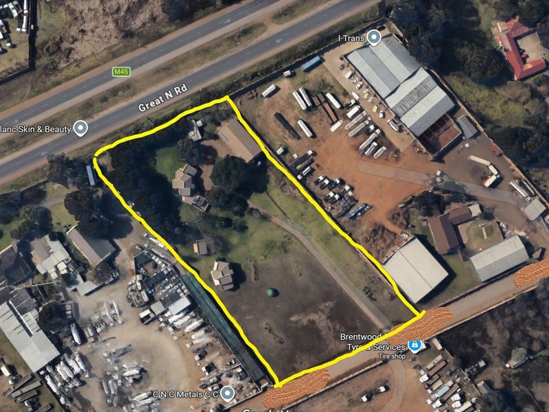 Aerial view of a commercial property plot with multiple structures, fenced boundaries, and direct access to Great North Road.