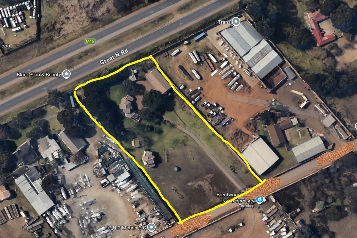 Aerial view of a commercial property plot with multiple structures, fenced boundaries, and direct access to Great North Road.