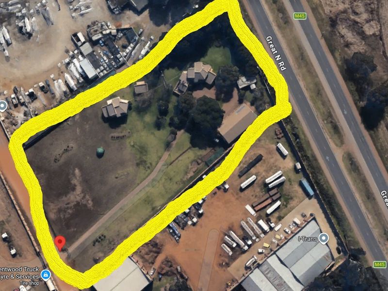 Aerial view of a commercial property site featuring multiple detached buildings, landscaped grounds, and paved access areas situated along a main road.