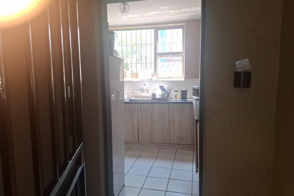 A view into a functional kitchen featuring built-in cabinetry, a stainless steel sink, and security bars on the window.