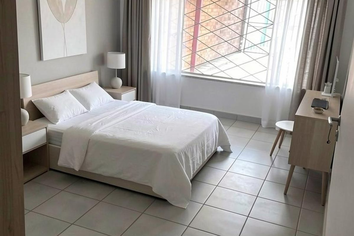 A well-maintained bedroom featuring neutral wall tones, tiled flooring, and a large window fitted with a security gate.
