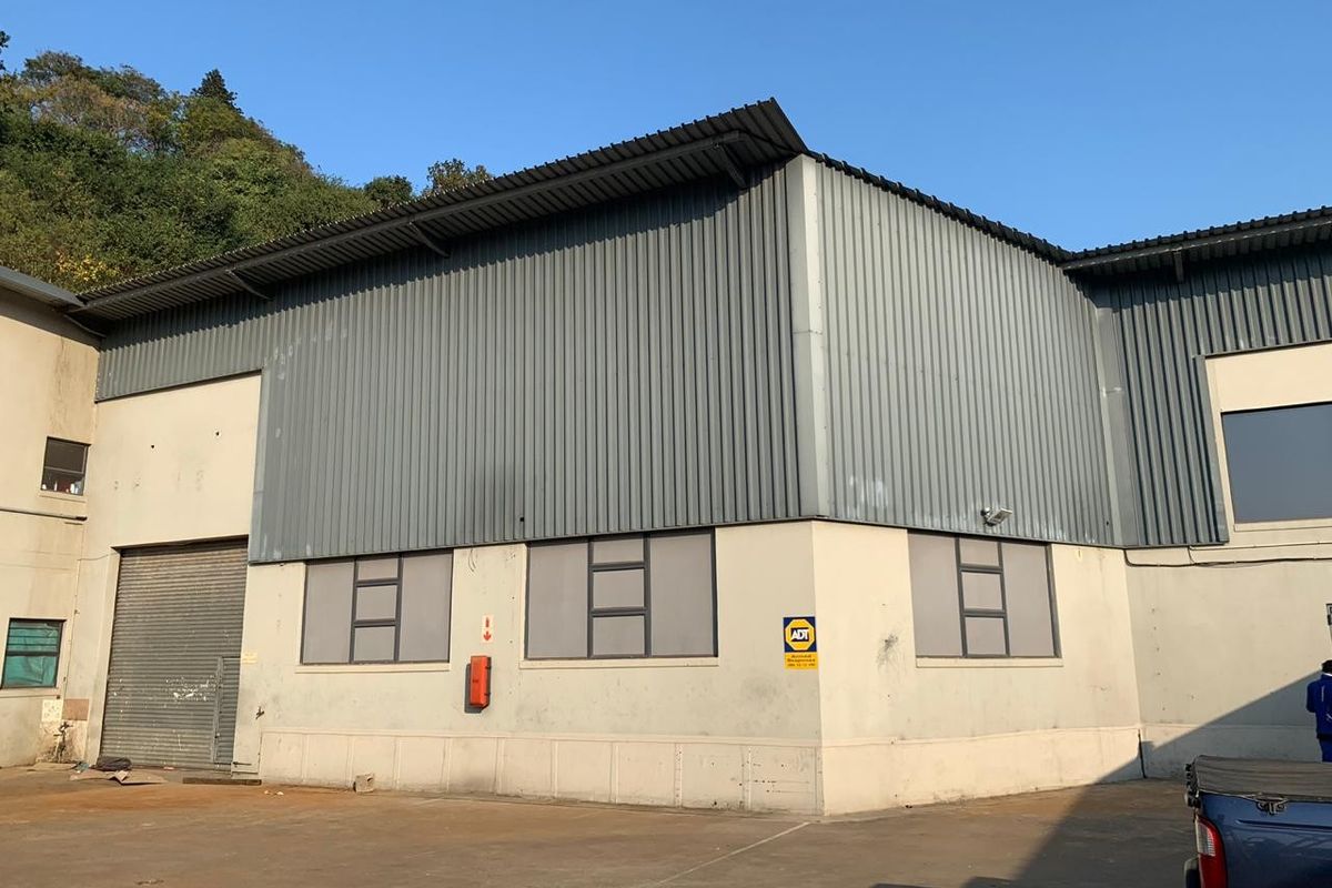 Exterior view of a commercial warehouse building featuring corrugated metal cladding, a roller shutter door, and security infrastructure.