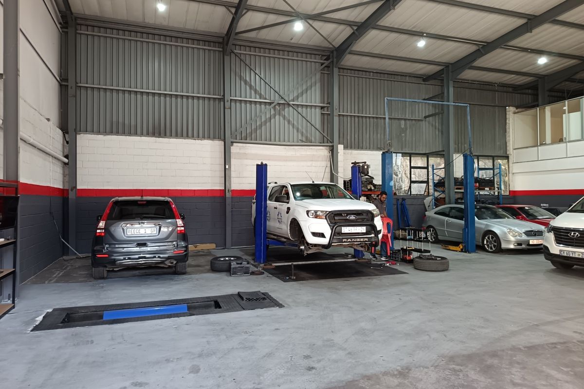 A functional commercial workshop featuring a two-post vehicle lift, in-ground inspection pit, and high-clearance industrial steel structure with durable concrete flooring.