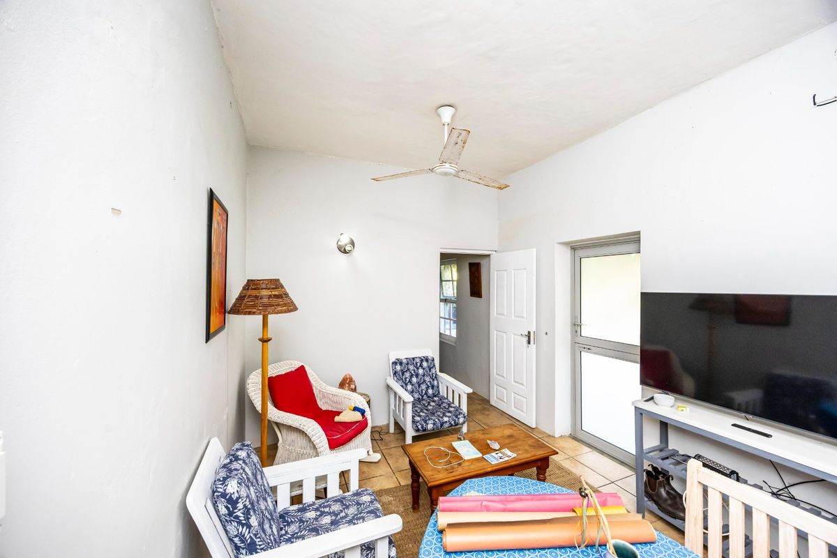 A functional living room featuring tiled flooring, a ceiling fan, and direct access to an outdoor area through a glass-paneled door.
