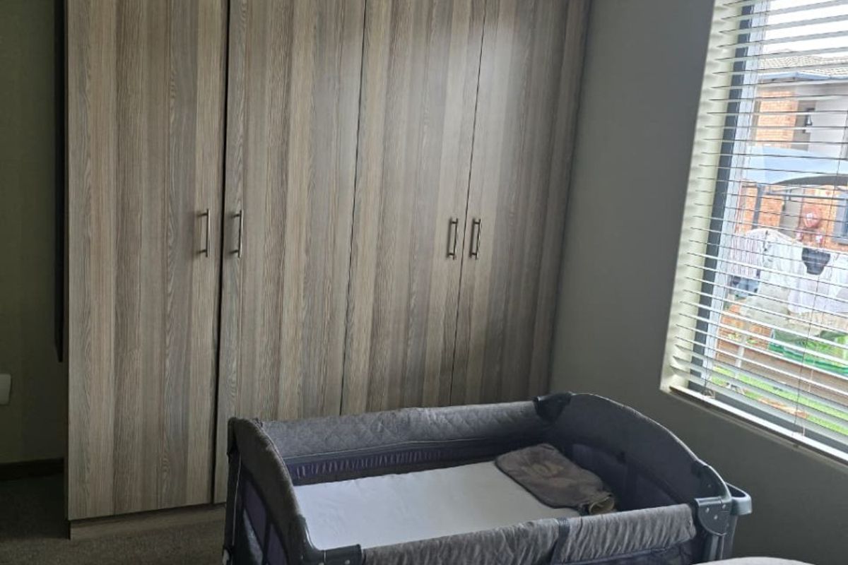 A bedroom featuring built-in wooden cupboards, carpeted flooring, and a window fitted with venetian blinds.