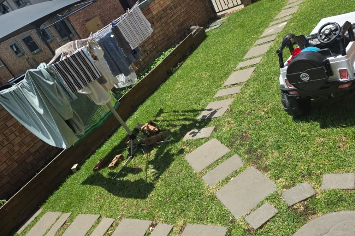 A private rear garden featuring a lawn, stone paver pathway, and brick boundary walls with overhead shade sails.