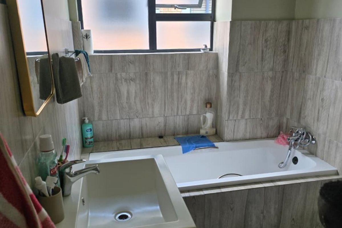 A modern bathroom featuring a built-in bathtub, vanity basin with mixer tap, and wood-look tiled wall finishes with a top-hung window.