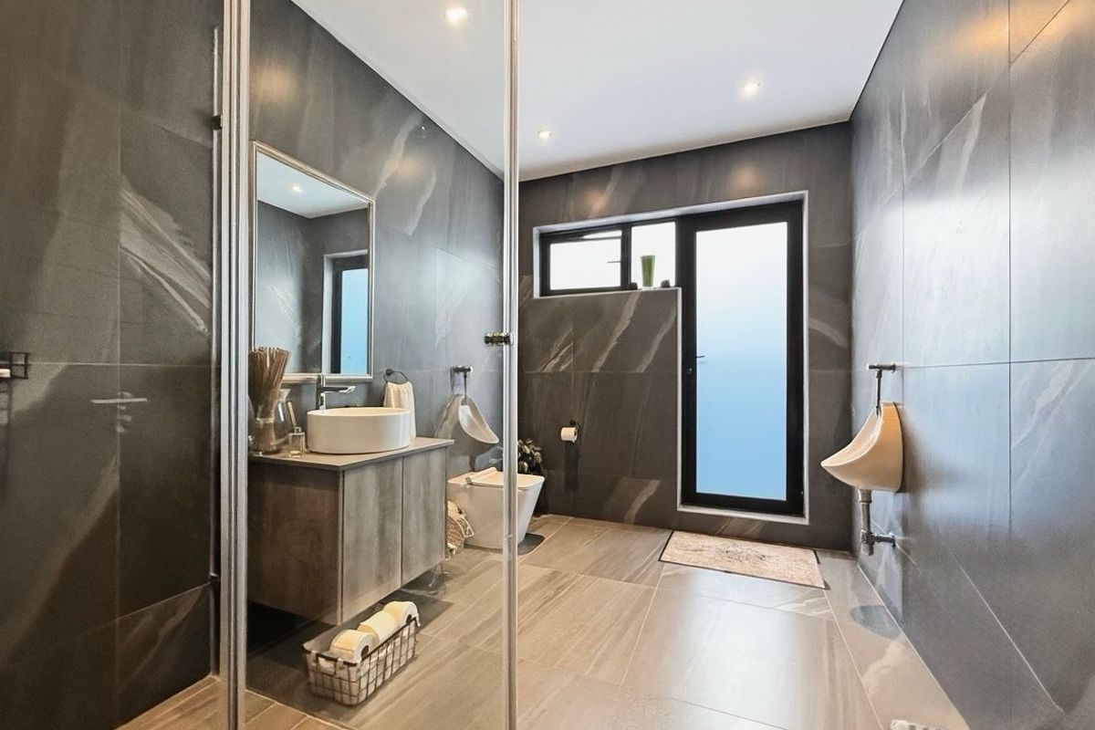 Modern bathroom featuring dark large-format wall tiles, a floating vanity with vessel sink, wall-mounted urinal, and a glass-enclosed shower area.