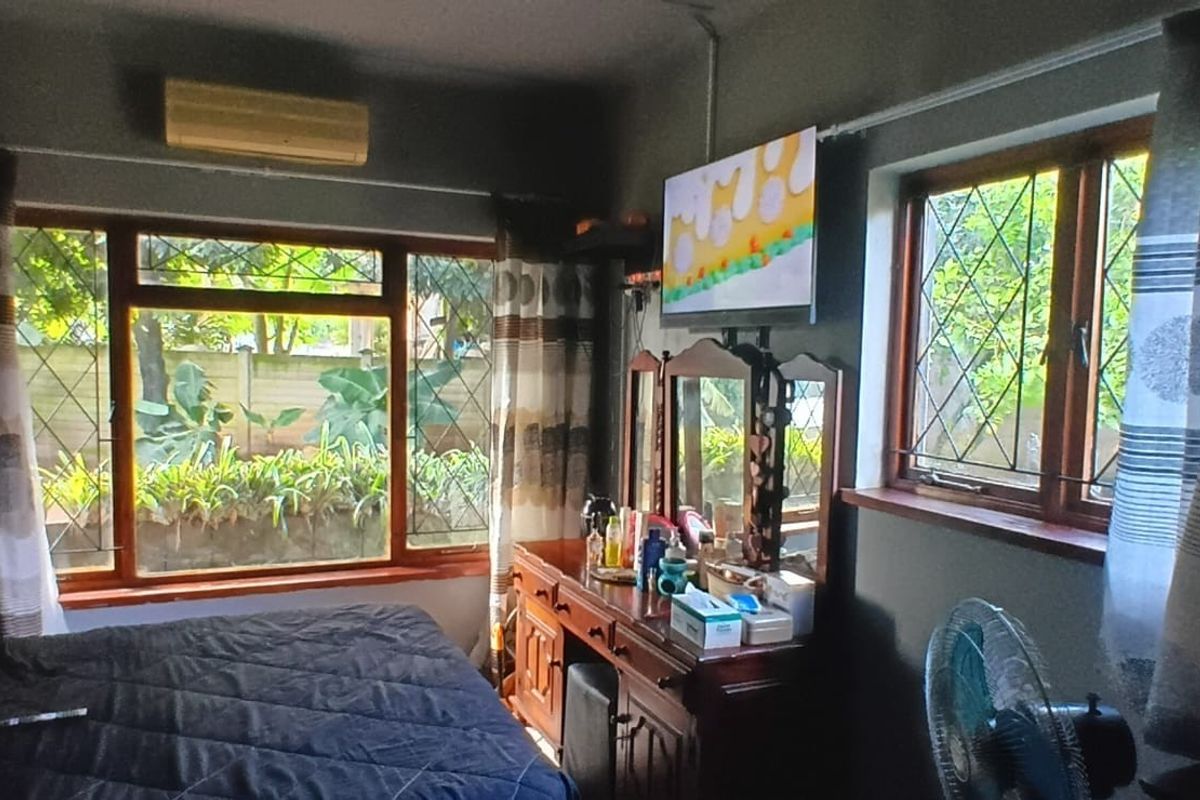 A bedroom featuring timber-framed windows with security bars, a wall-mounted air conditioning unit, and a wall-mounted television.