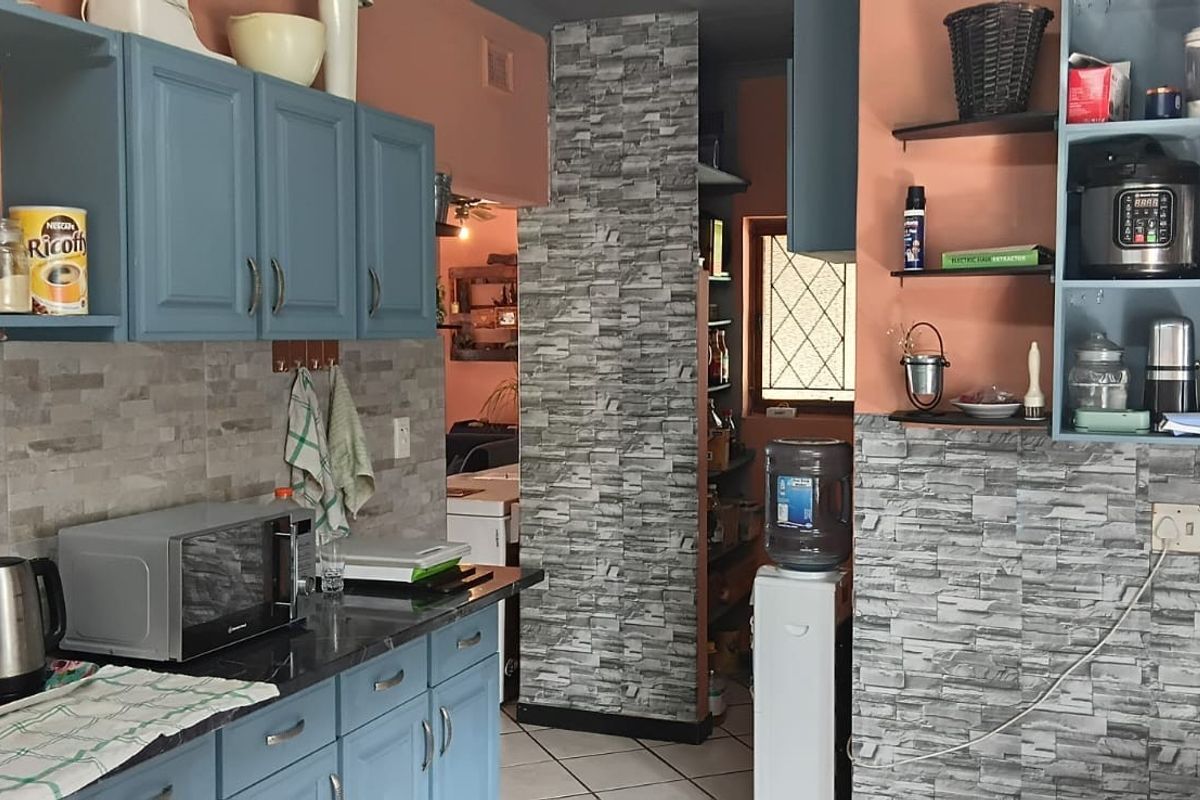 A functional kitchen featuring blue cabinetry, stone-look tiled splashbacks, and a dedicated scullery or pantry area with tiled flooring.