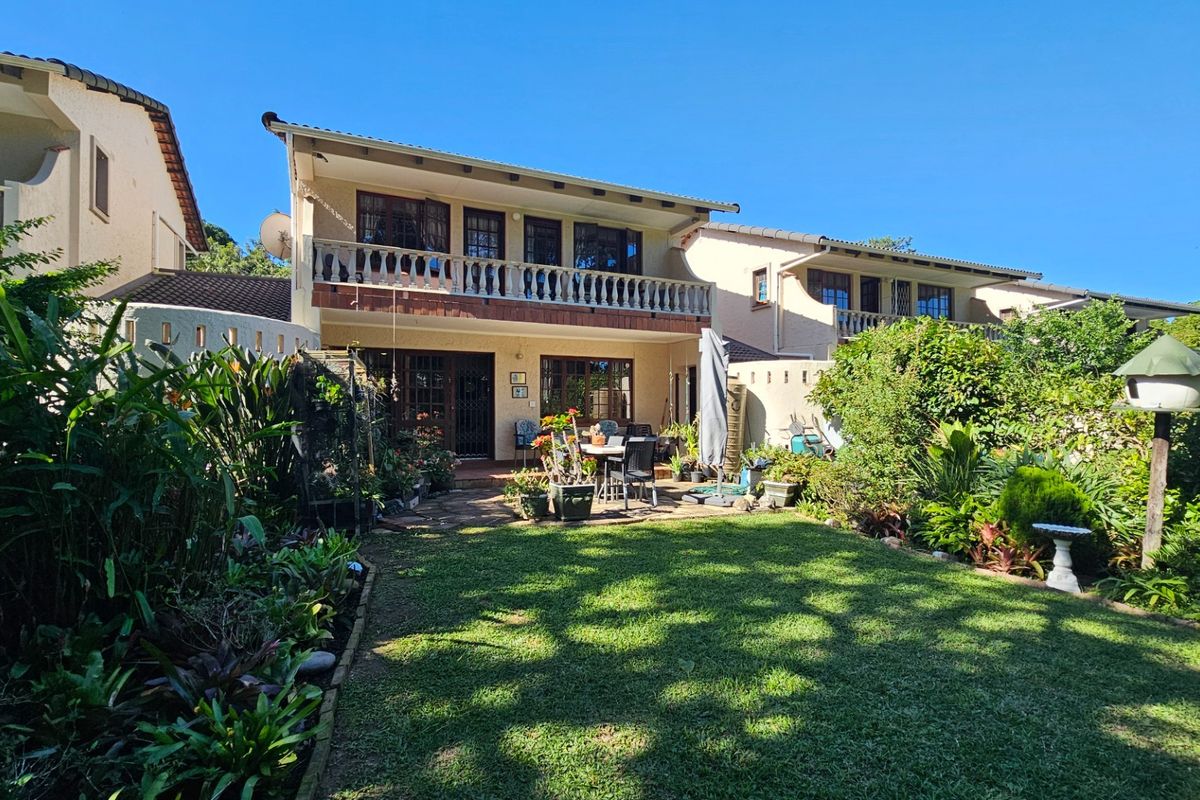 Rear view of the townhouse featuring a private garden, paved patio area, and an upper-level balcony with traditional balustrades.