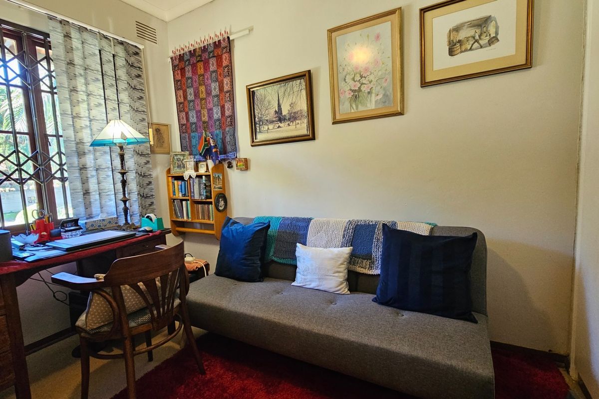 A multi-purpose room currently utilized as a home office and guest space, featuring a large window with security bars and neutral wall finishes.