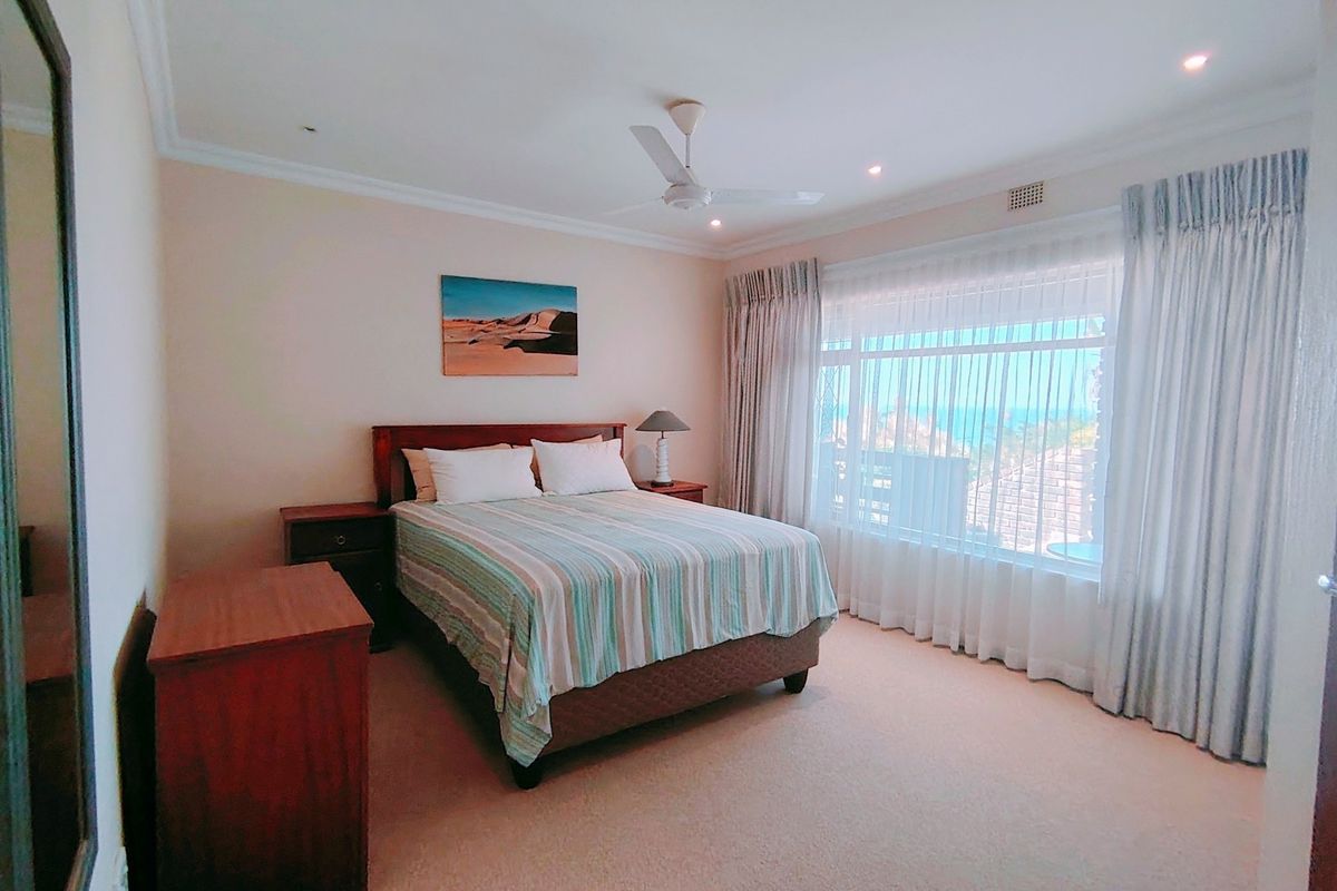 A well-maintained bedroom featuring neutral carpeting, recessed ceiling lighting, a ceiling fan, and large windows with curtains offering natural light.