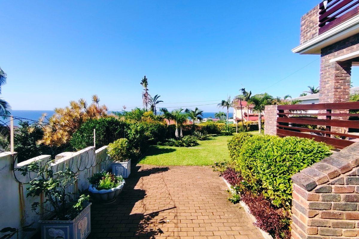 A well-maintained rear garden featuring a brick-paved patio, lush lawn, and established landscaping with a scenic coastal view.