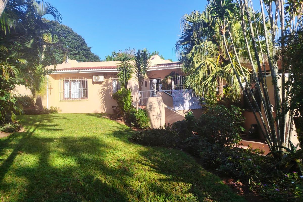A view of the rear elevation of the house featuring a well-maintained lawn, mature garden landscaping, and exterior security features.