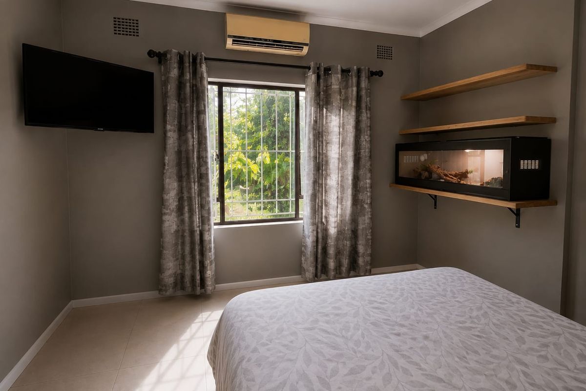 A well-maintained bedroom featuring tiled flooring, a split-system air conditioner, security bars on the window, and built-in wall shelving.