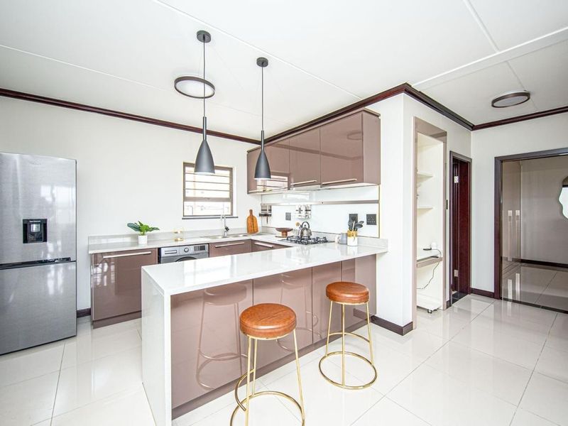 Modern kitchen featuring high-gloss cabinetry, stone countertops, a breakfast bar, and integrated gas hob, offering a sleek and functional culinary space.