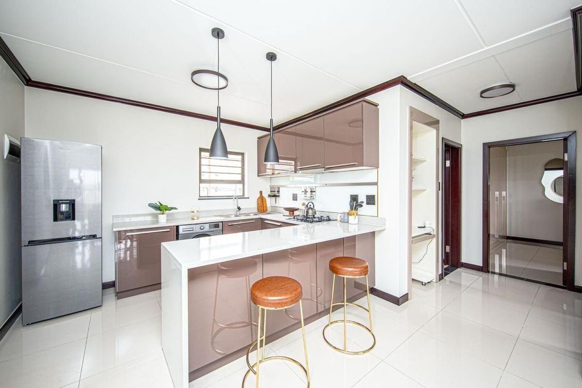 Modern kitchen featuring high-gloss cabinetry, stone countertops, a breakfast bar, and integrated gas hob, offering a sleek and functional culinary space.