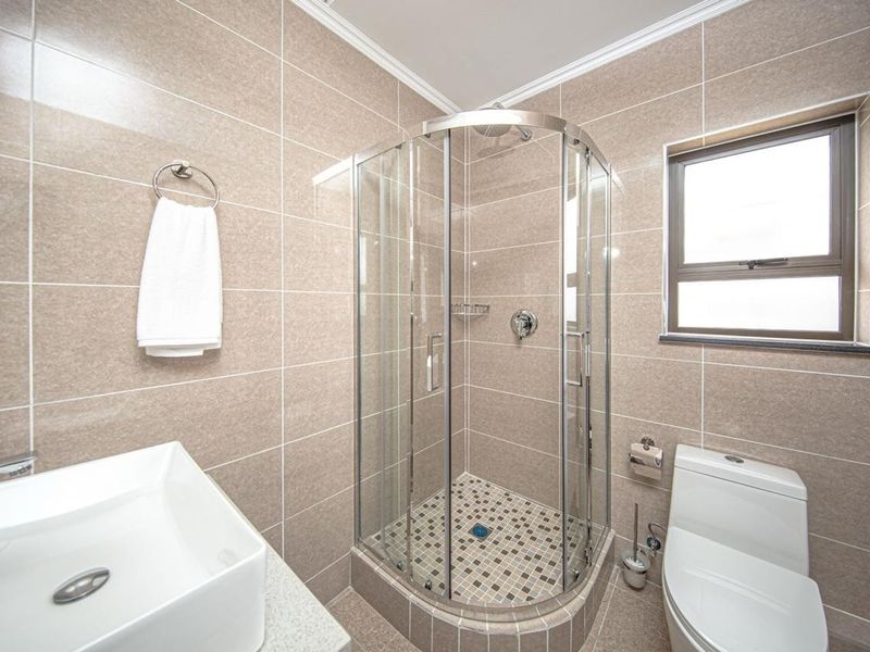 Modern bathroom featuring a corner glass shower enclosure, tiled walls, a contemporary vessel sink, and a standard toilet.