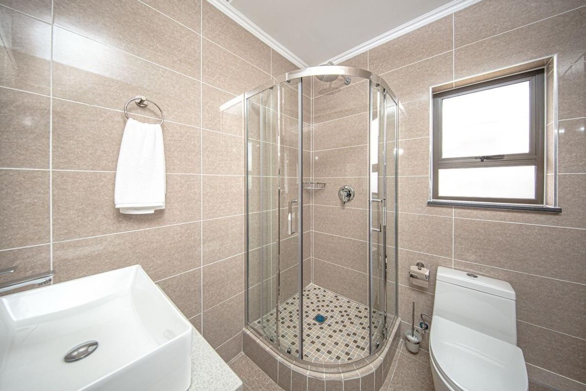 Modern bathroom featuring a corner glass shower enclosure, tiled walls, a contemporary vessel sink, and a standard toilet.
