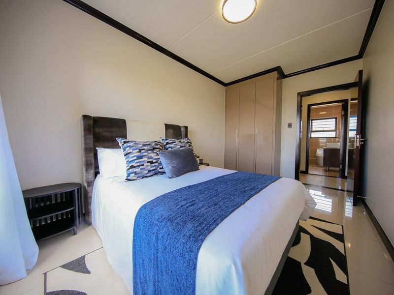 A well-maintained bedroom featuring built-in cupboards, tiled flooring, and an en-suite bathroom with modern finishes.
