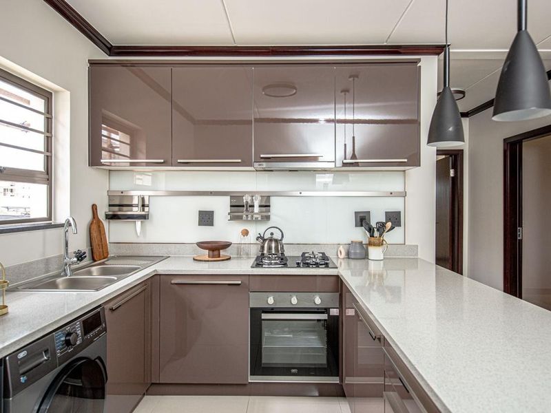 Modern kitchen featuring high-gloss cabinetry, stone countertops, integrated gas hob, built-in oven, and a double stainless steel sink with a breakfast bar.