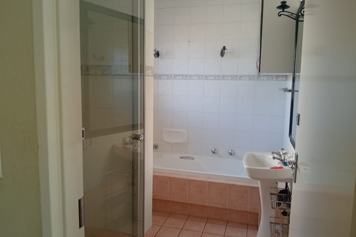 A functional bathroom featuring a built-in bathtub, pedestal sink, and a glass-enclosed shower area with tiled walls and flooring.