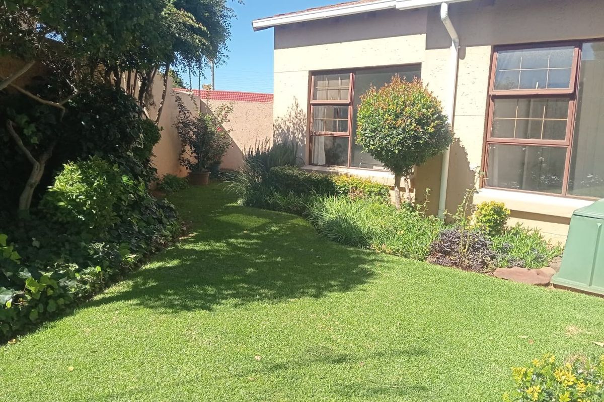 A well-maintained rear garden area featuring a manicured lawn, established perimeter landscaping, and views of the property's rear exterior wall and windows.