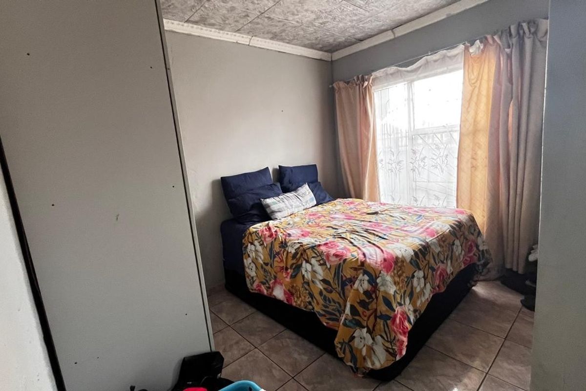 A compact bedroom featuring tiled flooring, a built-in cupboard, and a window with natural light.
