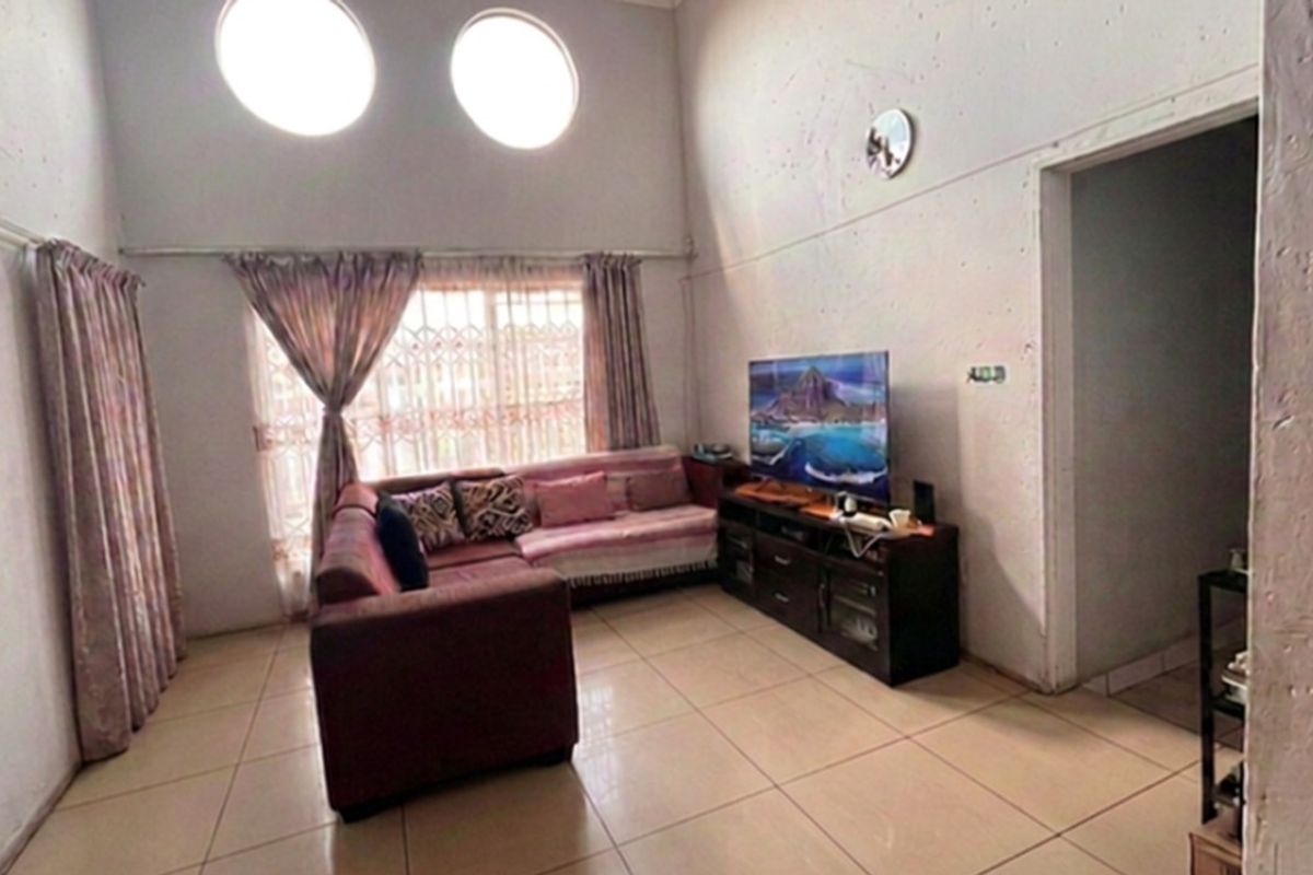 A living room featuring high ceilings with circular windows, tiled flooring, and a large window with security gate.