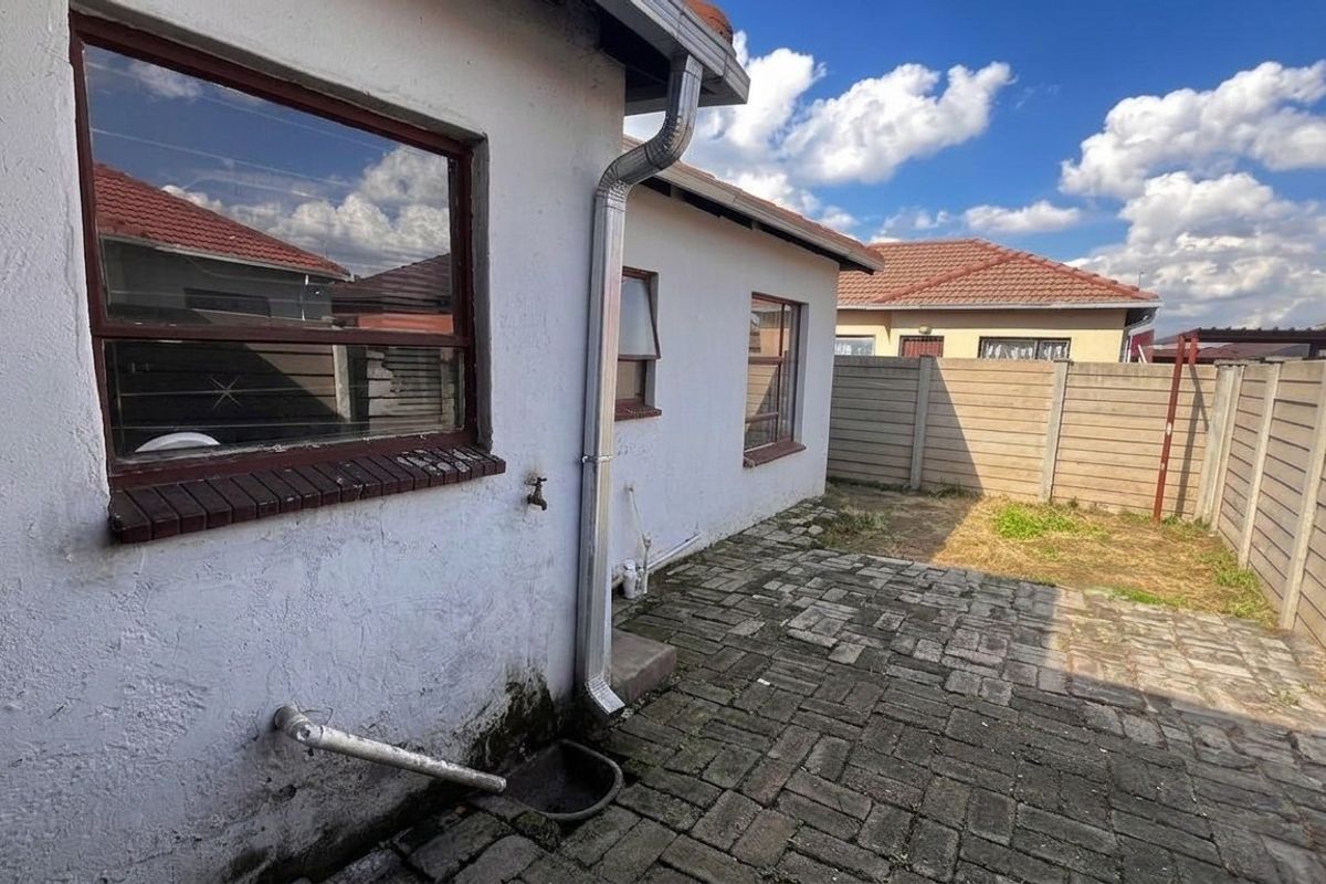 Rear exterior view of the property featuring a paved courtyard, perimeter walling, and external plumbing fixtures.