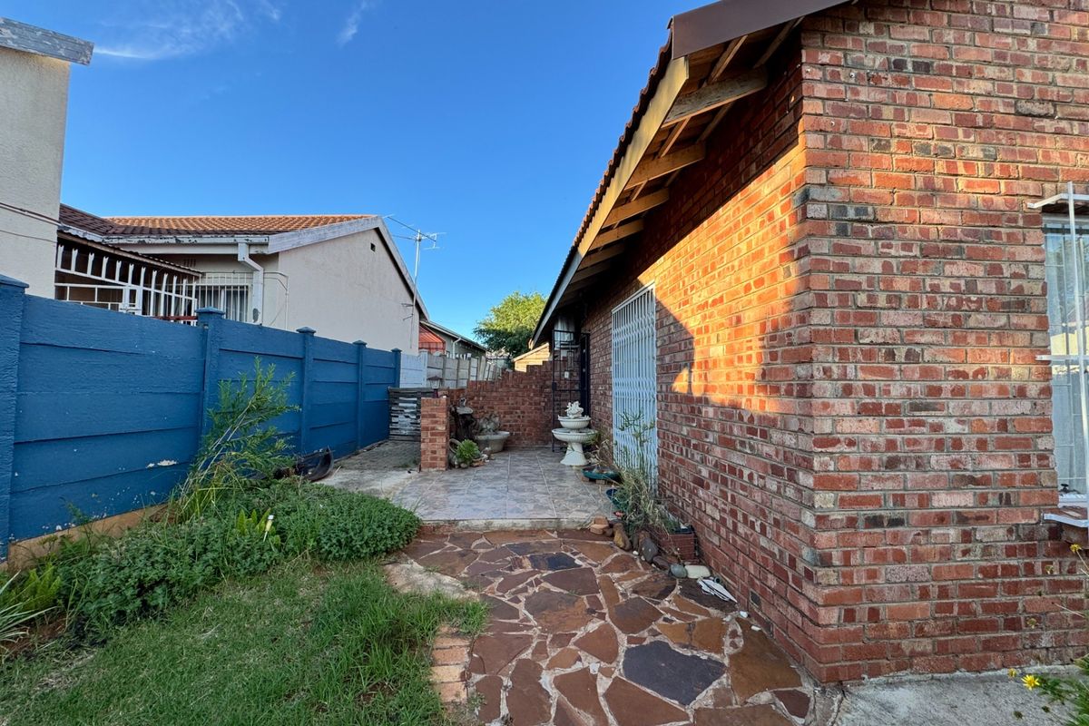 A rear exterior view of the property featuring a brick facade, stone paved pathway, and a small patio area with a boundary wall.