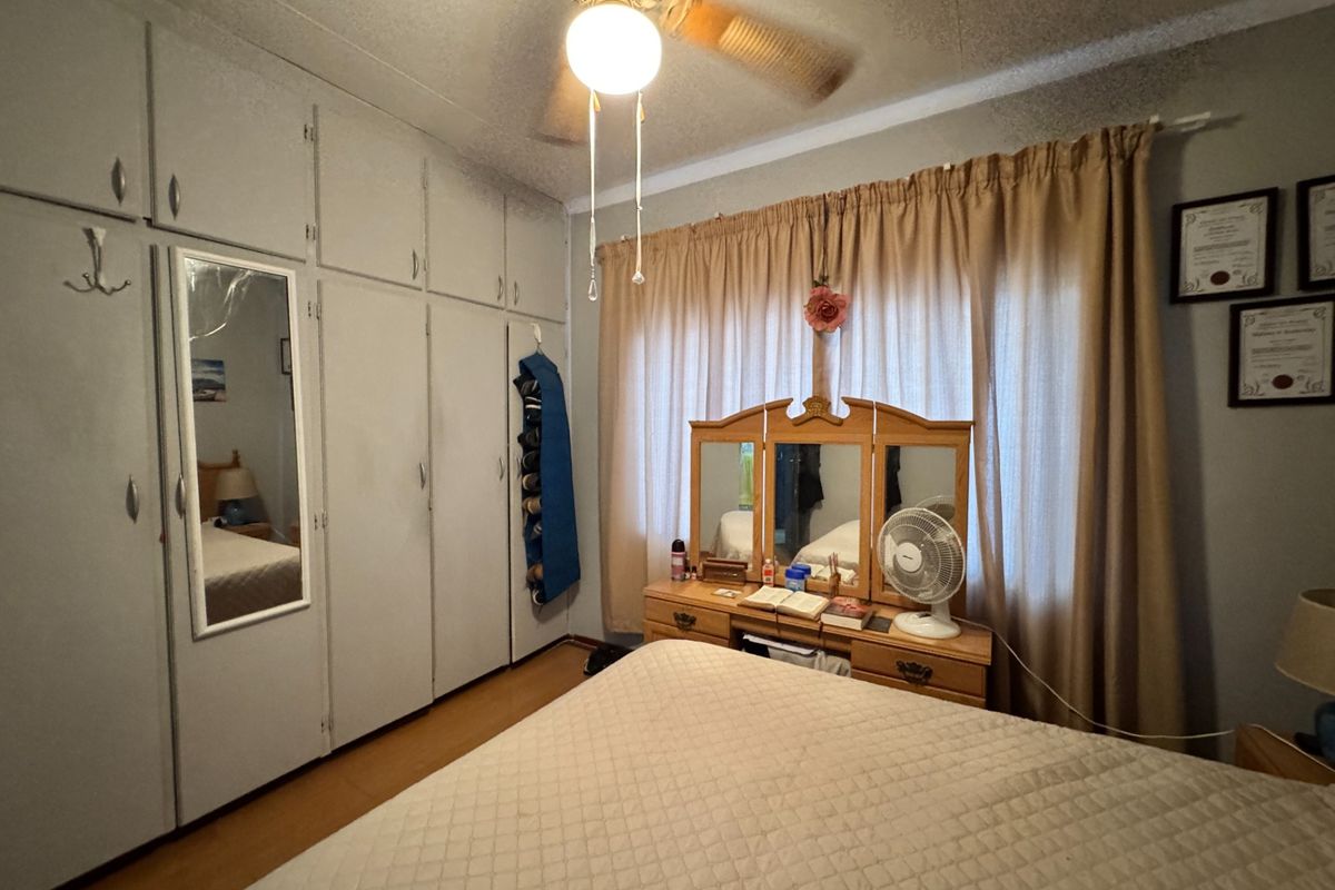 A bedroom featuring extensive built-in floor-to-ceiling cabinetry, a ceiling fan, and large window with curtains.
