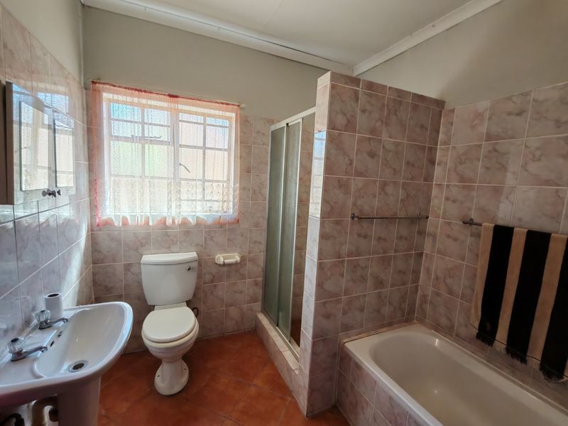A functional bathroom featuring a built-in bathtub, separate shower enclosure, pedestal basin, and toilet with dated ceramic wall tiling.