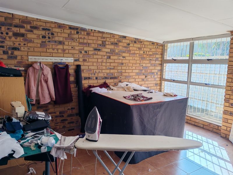 A multi-purpose utility room featuring exposed brick walls, tiled flooring, and large windows with security bars, suitable for a home office or hobby space.