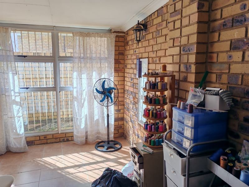 A sunlit enclosed patio or utility space featuring exposed face-brick walls, tiled flooring, and large windows with security bars.