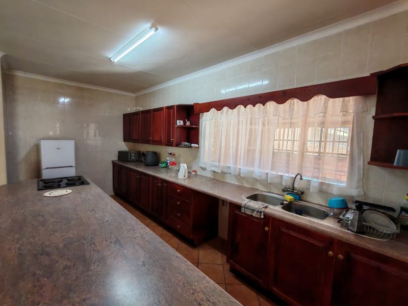 A functional kitchen featuring dark wood cabinetry, tiled walls, a double basin sink, and a large breakfast bar counter.