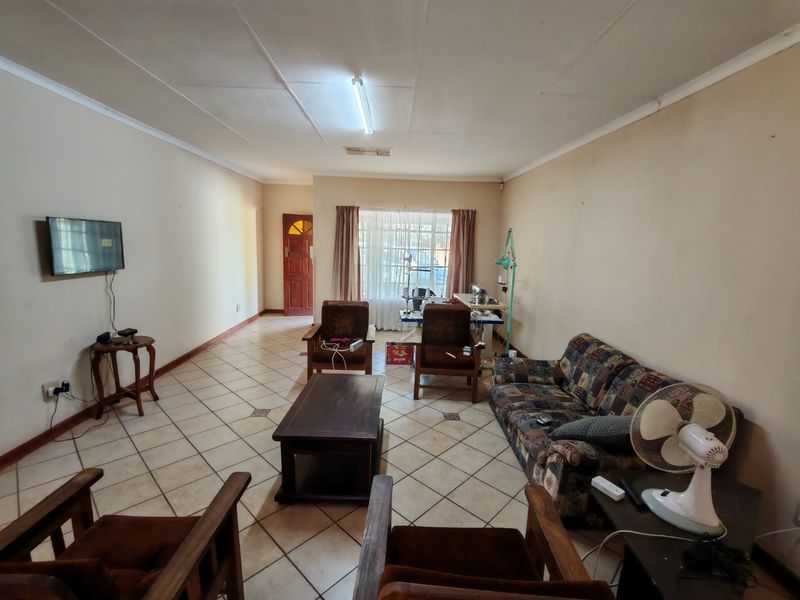 A spacious living room featuring ceramic floor tiles, a large window with natural light, and a solid timber entrance door.