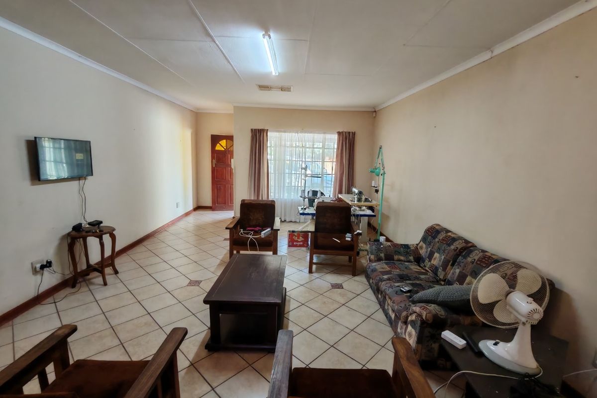 A spacious living room featuring ceramic floor tiles, a large window with natural light, and a solid timber entrance door.