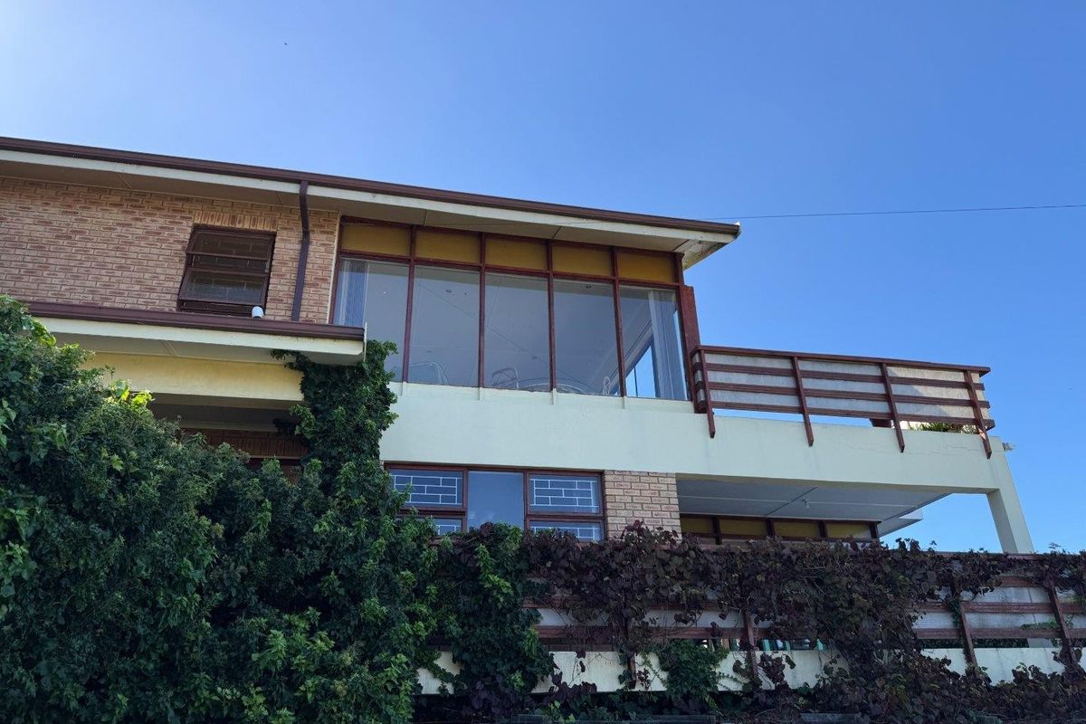 Rear exterior view of a multi-level house featuring a large enclosed sunroom, timber balcony railings, and brick facade elements with established climbing vegetation.